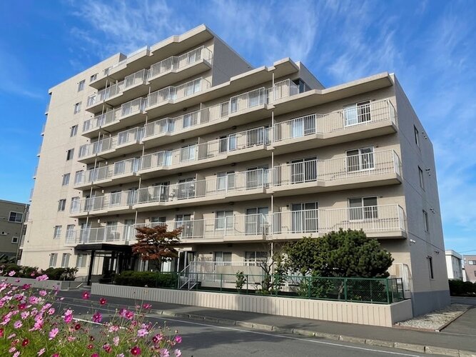 青空に映える落ち着いた色合いの重厚感ある外観デザイン！敷地内には緑豊かな植栽が整えられており、心地よいアプローチを演出します。周辺環境とも調和した美しい佇まいが日々の帰宅を迎えてくれます