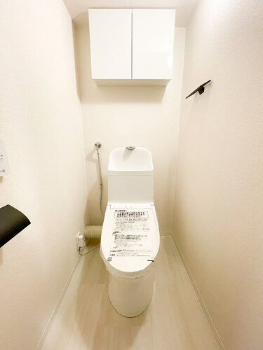 白を基調とした清潔感あふれる温水洗浄便座付きのトイレです！上部にはトイレットペーパーなどを目隠しして収納できる便利な吊戸棚が備わっています。床や壁もスッキリとしており、毎日気持ちよく使えます♪